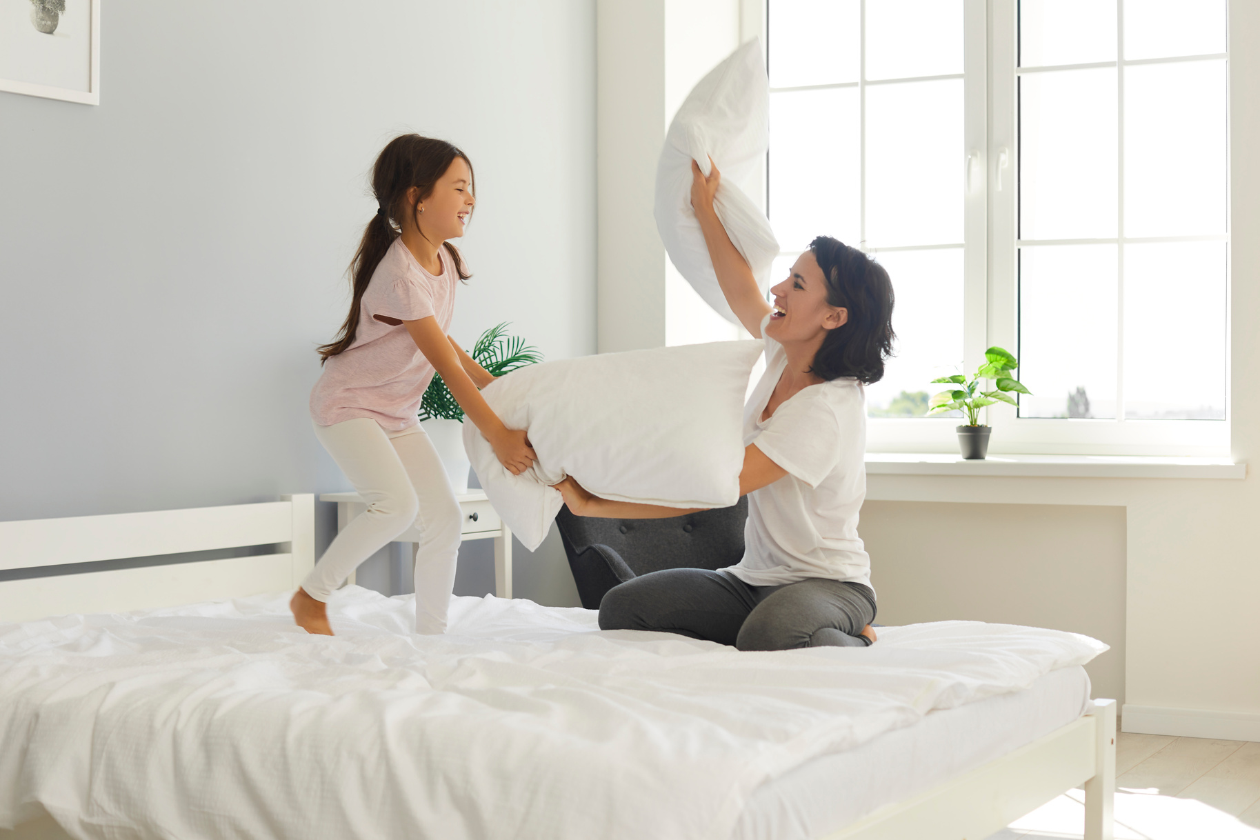 Cheerful Mummy and Cute Little Daughter Fighting with Pillows on Wide Bed at Home